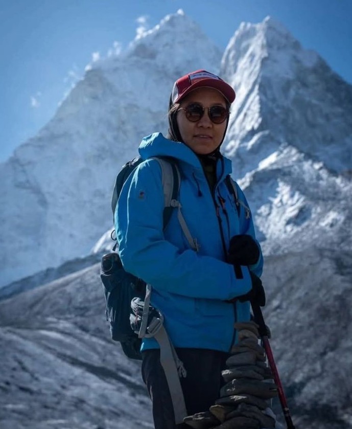 Chhonzin Angmo, wearing a blue jacket, sunglasses, and a red cap standing in front of Mount Everest.
