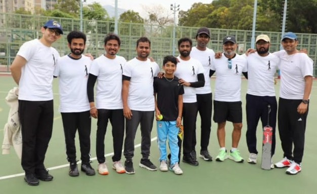 A group of cricket players from the Hong Kong Indian community during HTBF Cricket Tournament 2025, wearing white t-shirts. A young boy stands in 
					front, and a cricket bat rests on the ground.