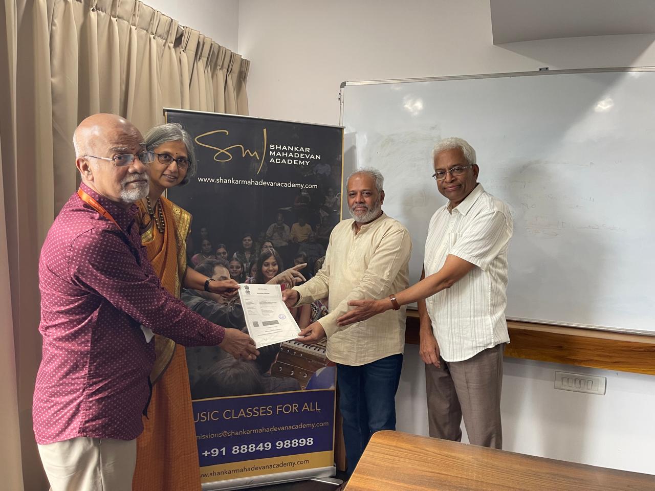 Photo of HTBF Trustees Ms. Deepa Krishnamoorthy, Mr. Sivaji Rao, and Mr. Nataraj Sankaran holding a signed MoU with a dignitary from the Shankar Mahadevan Academy