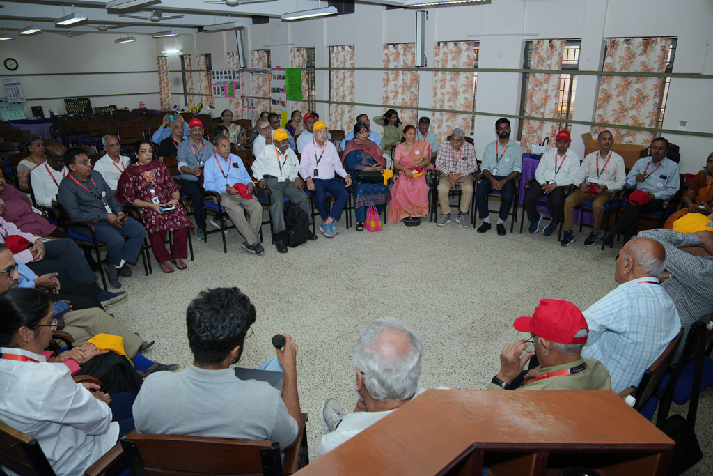 A group photo HTBF Trustees, staff, trainers, and volunteers sit in a large circle, listening attentively as a participant speaks into a microphone during a group discussion.